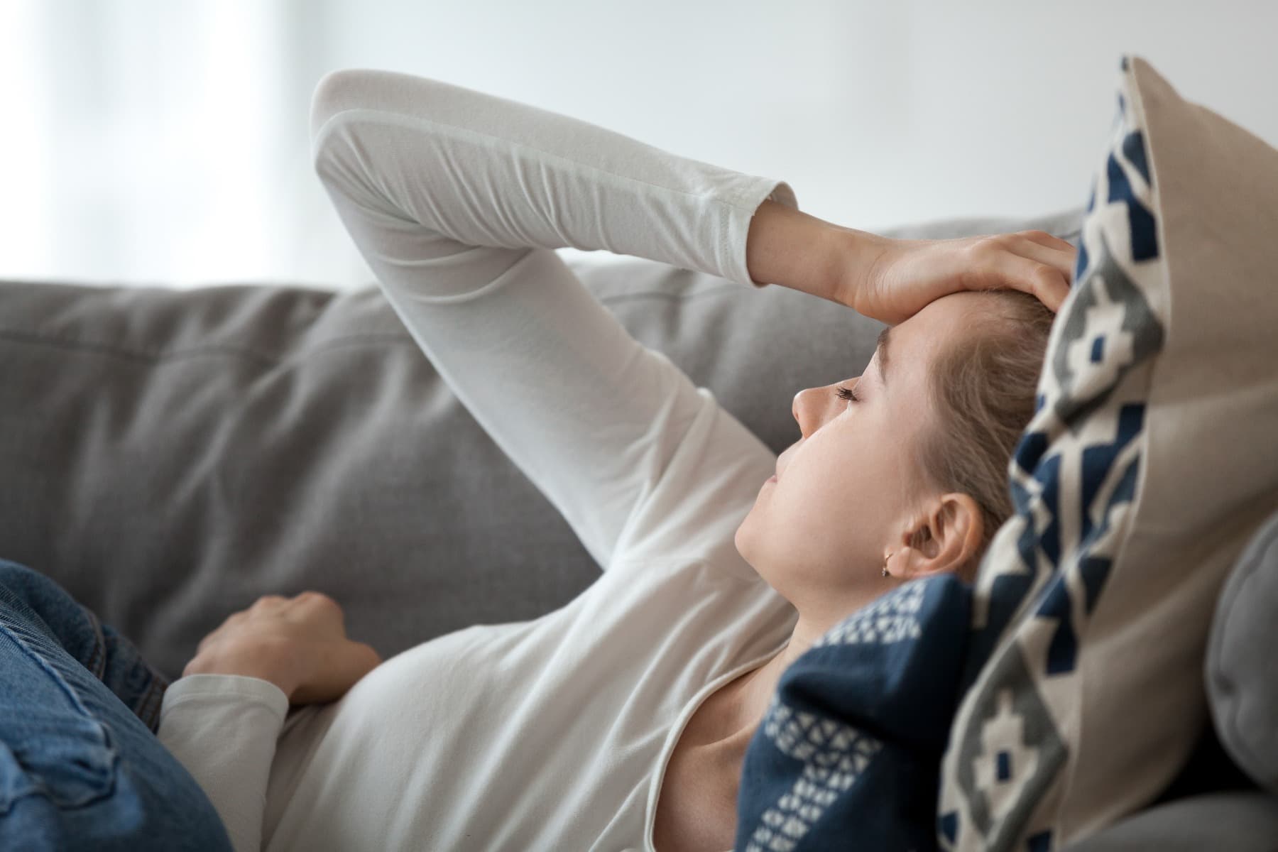 A lady clutching her head whilst laying on a sofa