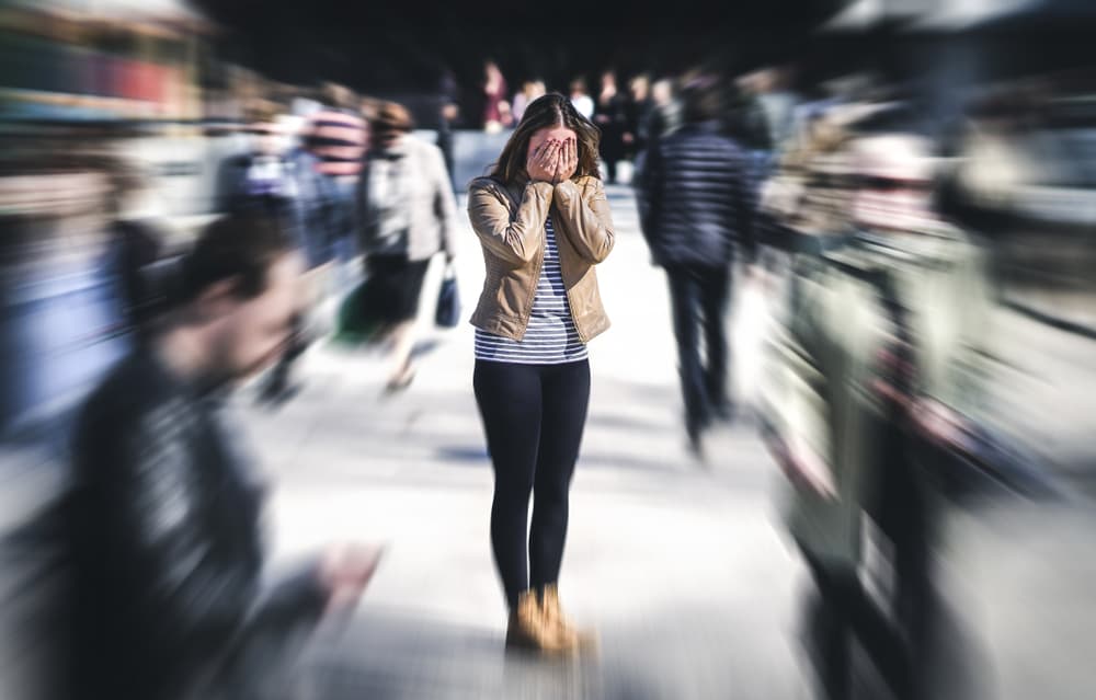 A lady in a large crowd covering her face due to experiencing situational anxiety