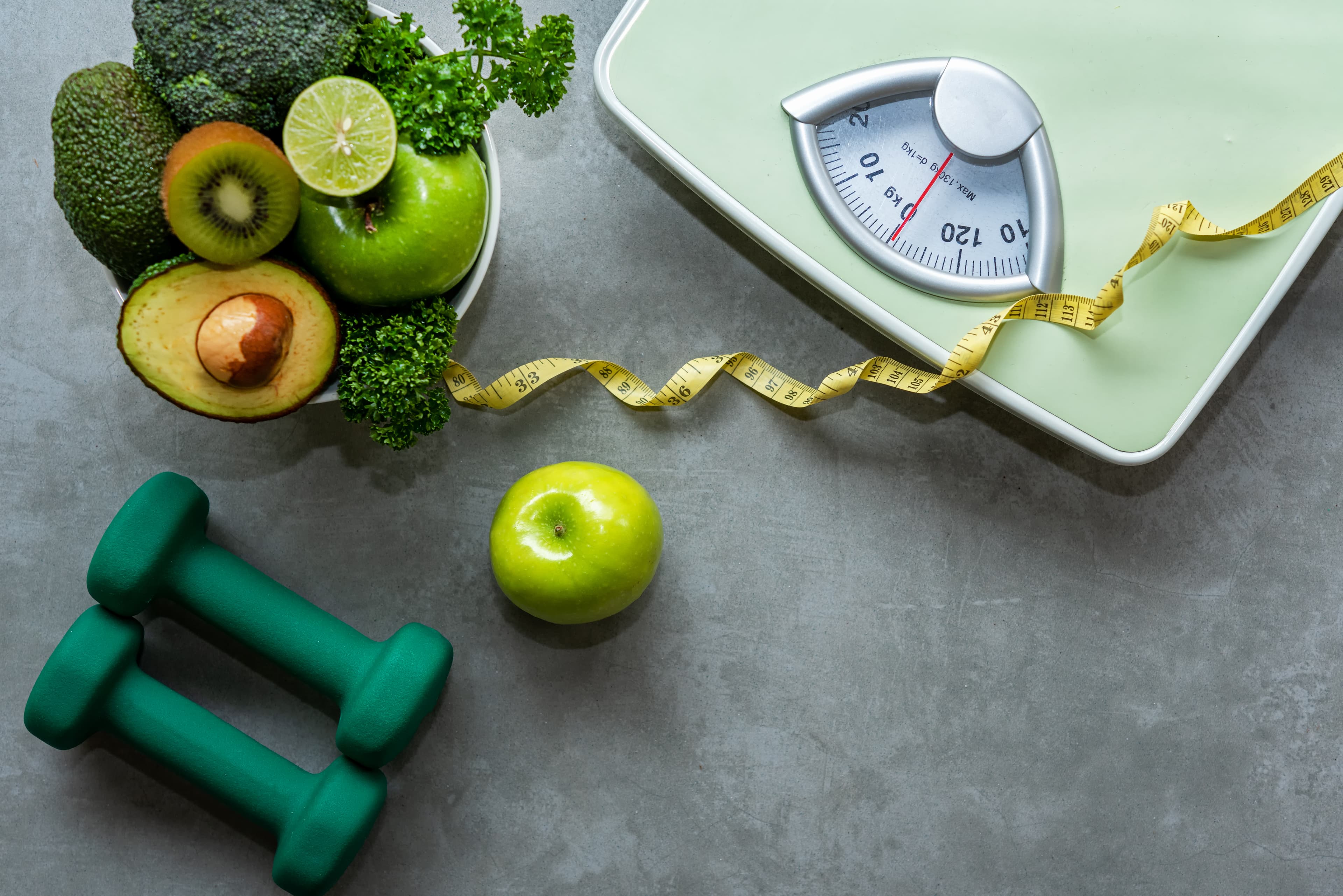 Fruits and vegetables next to some weighing scales and a pair of dumbbells