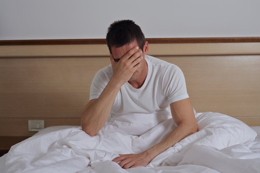 Man sitting up in bed struggling to sleep